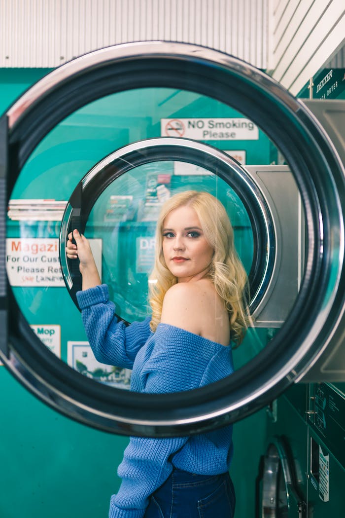 Elegant woman posing through a washer door in a fashionable laundromat setting.